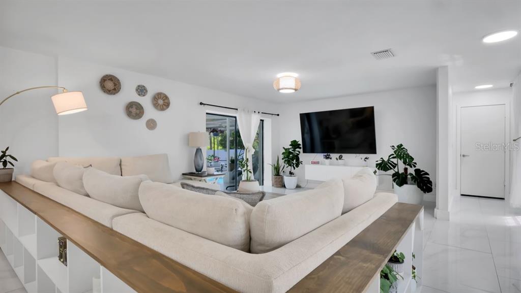 A bright living room features white tile floors, a large sectional sofa, and a front door — 1307 NORMANDY CIRCLE, PALM HARBOR, FL