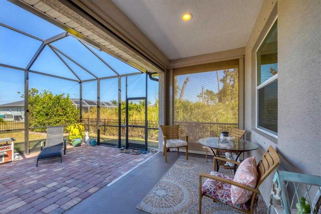 A screened-in patio features a brick paver floor, outdoor furniture, and a view of landscaping — 112 BERYL DRIVE, ROTONDA WEST, FL