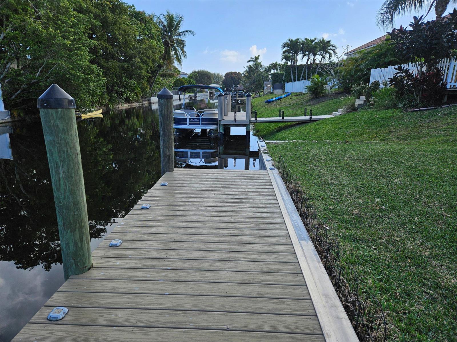 A wooden dock extends into a canal with a pontoon boat moored nearby — 1105 Anchor Point, Delray Beach FL 33444, DELRAY BEACH, FL