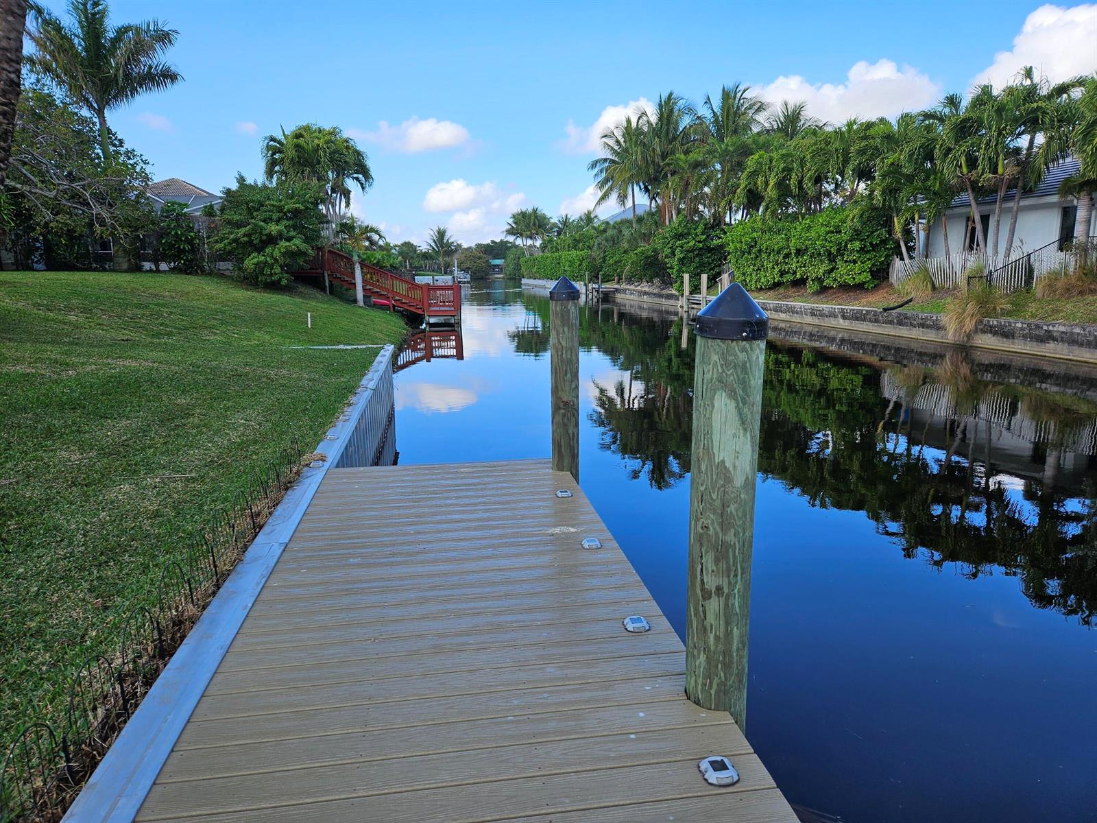 A wooden dock extends into a calm canal lined with palm trees and residential properties — 1105 Anchor Point, Delray Beach FL 33444, DELRAY BEACH, FL