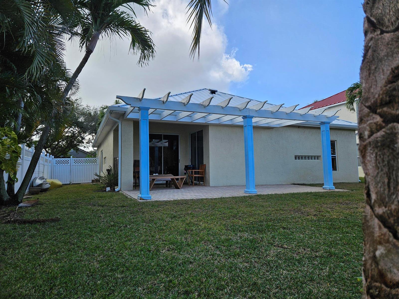A backyard patio features a white pergola supported by three blue columns against a house — 1105 Anchor Point, Delray Beach FL 33444, DELRAY BEACH, FL