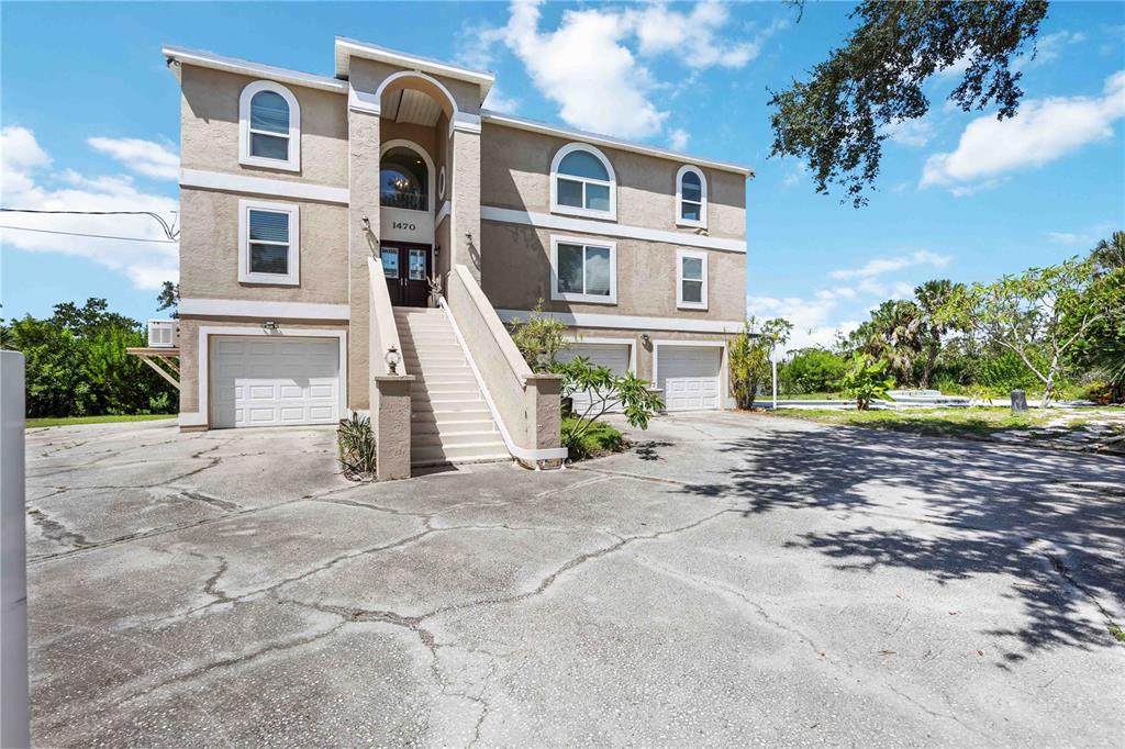 A three-story house with a raised entrance, multiple garage doors, and a cracked concrete driveway — 1470 BAYSHORE DRIVE, TERRA CEIA, FL