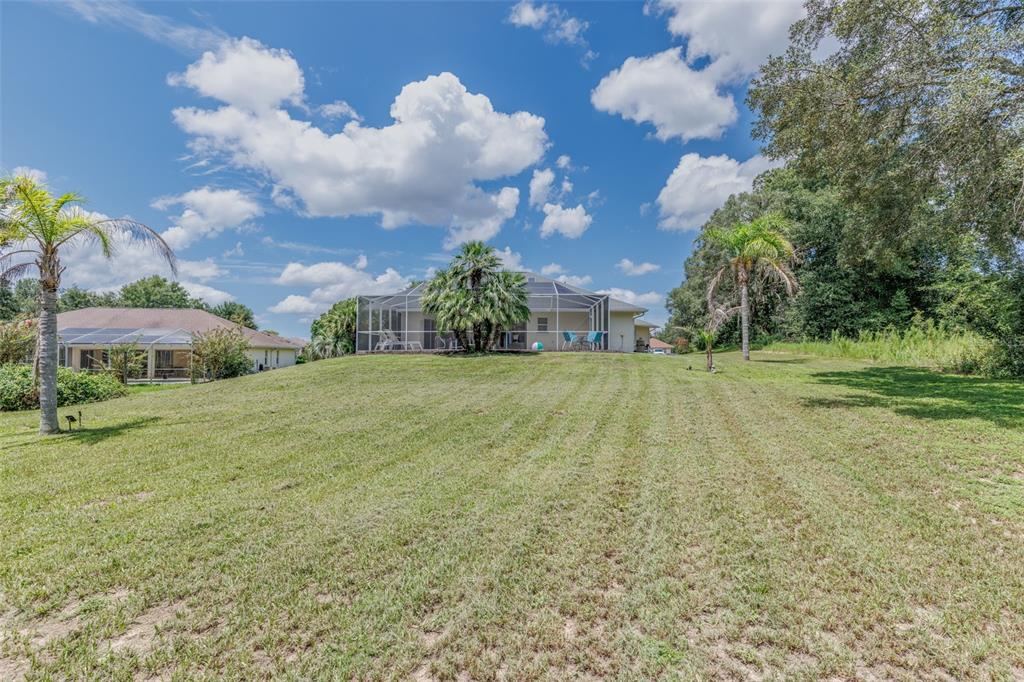A view of a house with a screened-in pool enclosure and a large grassy yard — 893 N BENNINGTON TERRACE, INVERNESS, FL