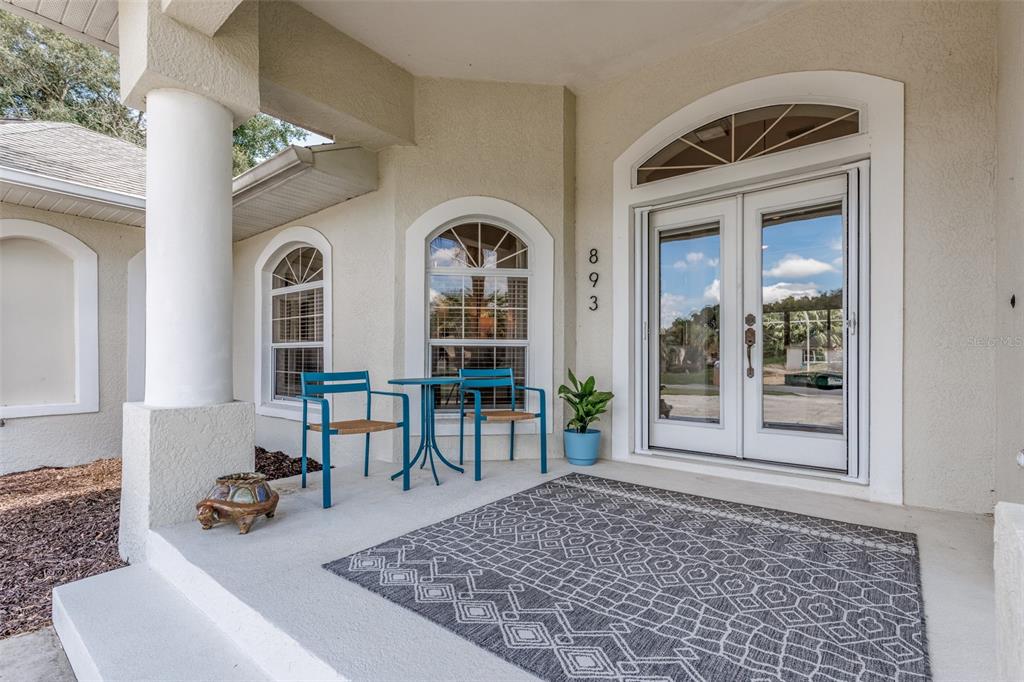 A covered front porch features a patterned rug, two blue chairs, and a double door — 893 N BENNINGTON TERRACE, INVERNESS, FL