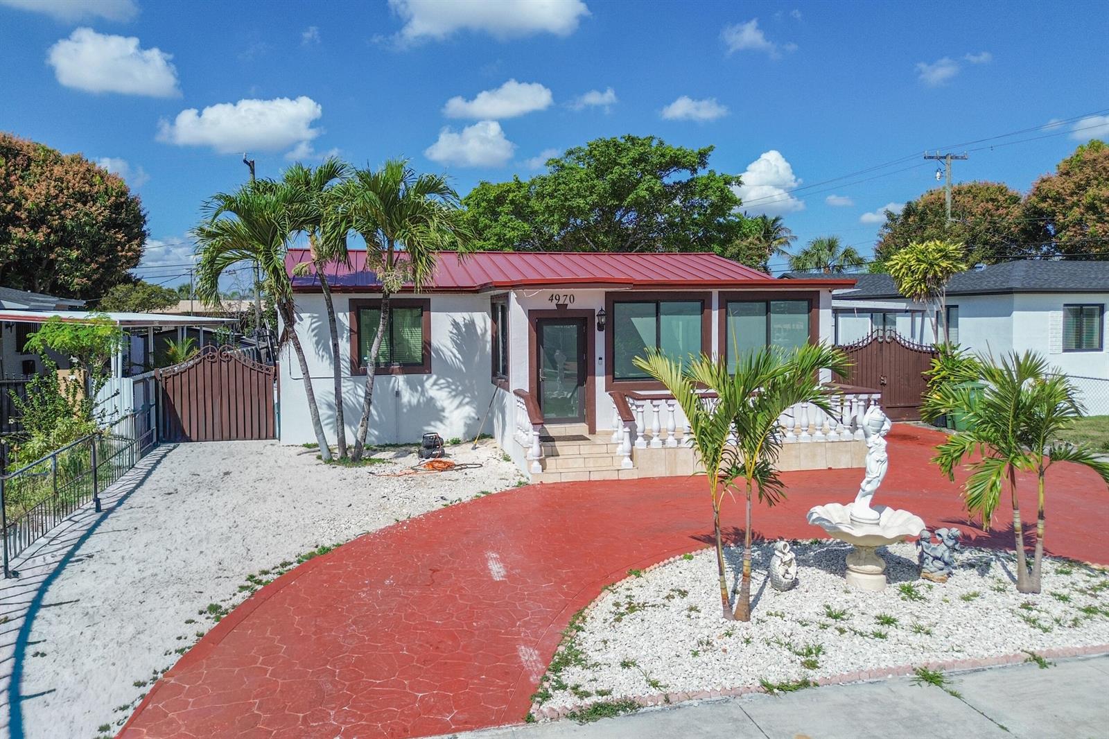 A single-story house with a red metal roof, white exterior, and a red paved driveway — 4970 E Palm Court, Hialeah FL 33013, HIALEAH, FL