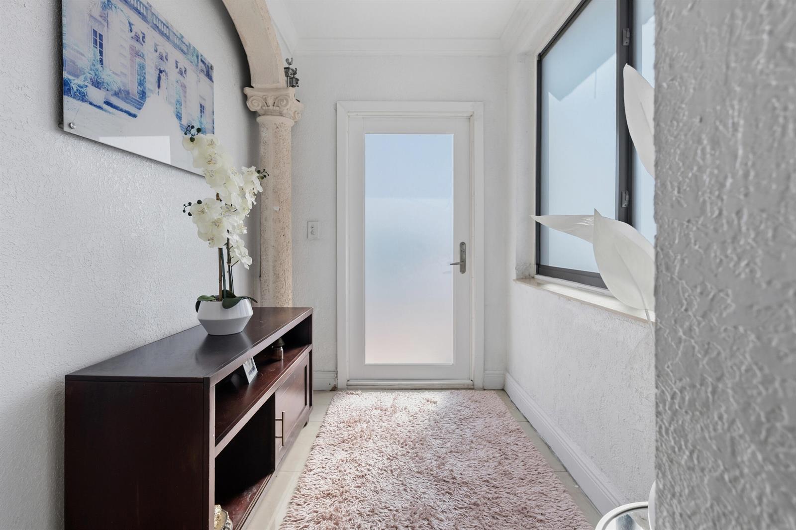 A bright entryway features a dark wood console table, a pink rug, and a stone column — 4970 E Palm Court, Hialeah FL 33013, HIALEAH, FL