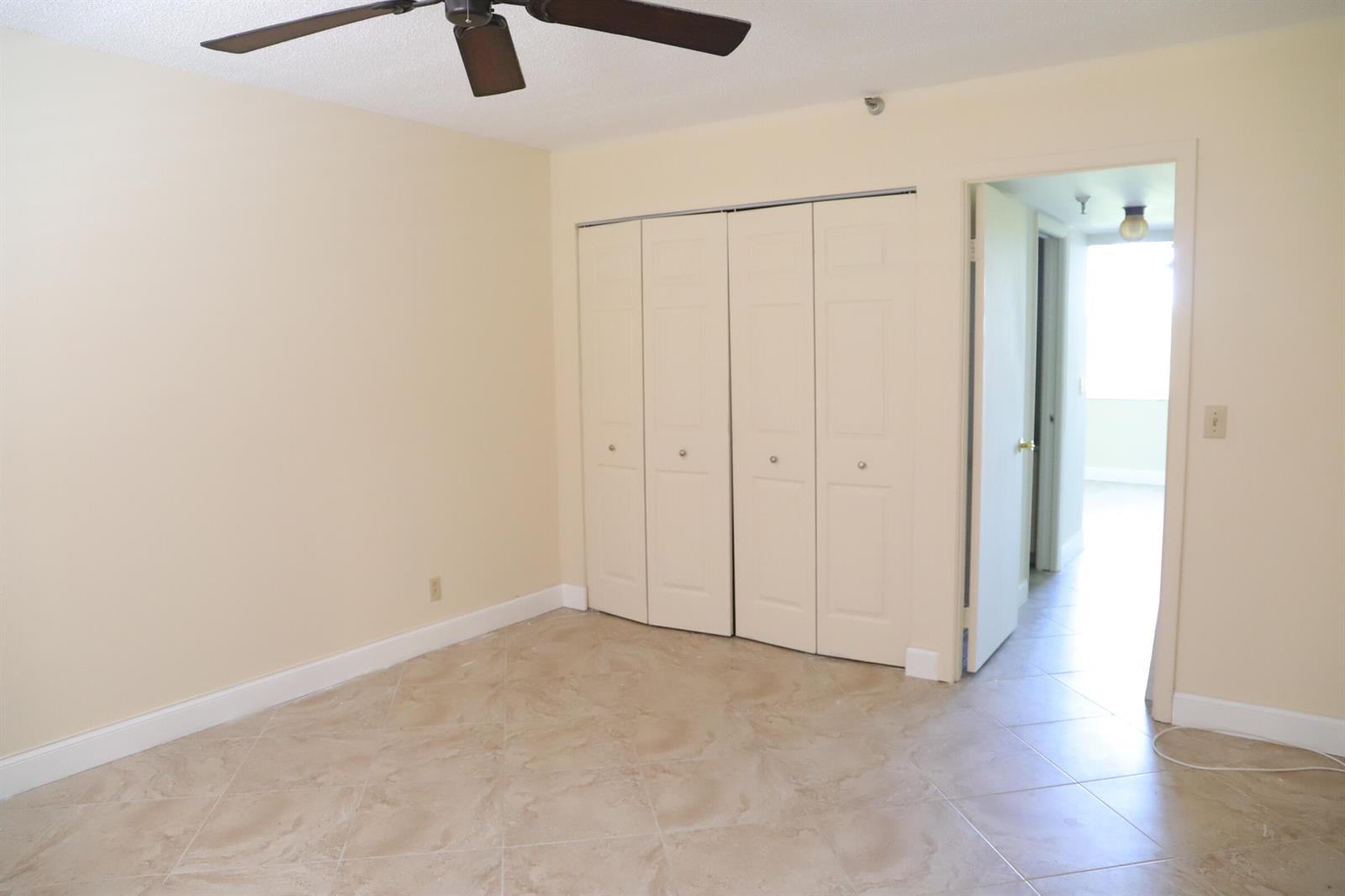 An empty bedroom with beige walls, tile flooring, a ceiling fan, and a closet — 6400 NW 2nd Avenue # 423, Boca Raton FL 33487, BOCA RATON, FL