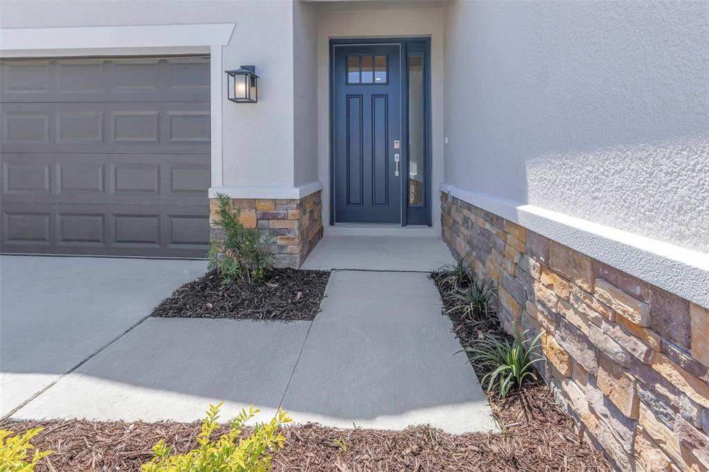 A concrete walkway leads to a blue front door beside a stone-accented garage exterior — 2676 LEAFWING COURT, PALM HARBOR, FL