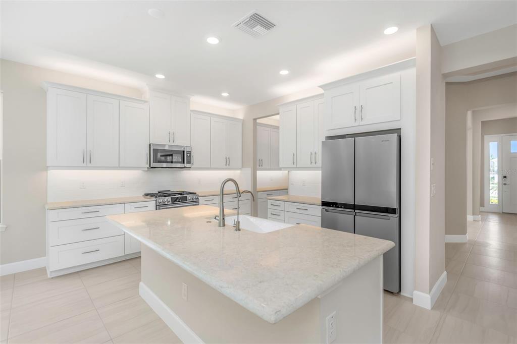 A modern kitchen features white cabinetry, stainless steel appliances, and a large central island — 2676 LEAFWING COURT, PALM HARBOR, FL