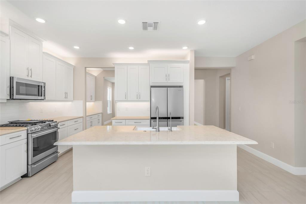A modern kitchen features white cabinets, stainless steel appliances, and a large central island — 2676 LEAFWING COURT, PALM HARBOR, FL