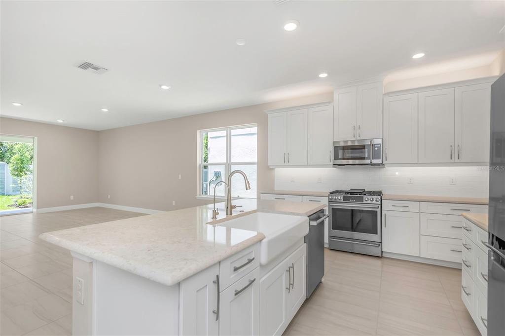 A modern kitchen features white cabinetry, a farmhouse sink, and a large stone-topped island — 2676 LEAFWING COURT, PALM HARBOR, FL