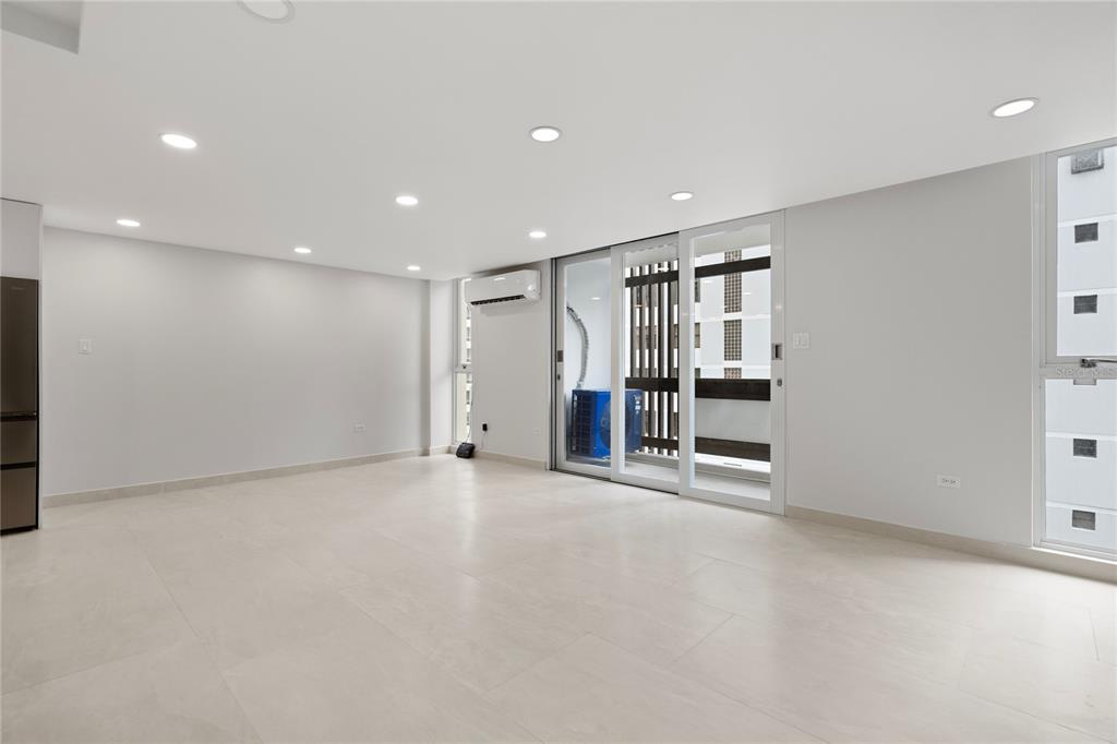 A bright, empty room features white tile flooring, recessed lighting, and a sliding glass door — 1407 ASHFORD AVENUE UNIT 5D, SAN JUAN, PR