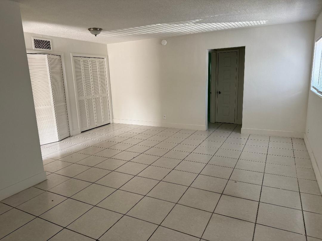 An empty room features white walls, light-colored tile flooring, and two sets of louvered closet doors — 1913 NE 2nd Street # 1, Pompano Beach FL 33060, POMPANO BEACH, FL