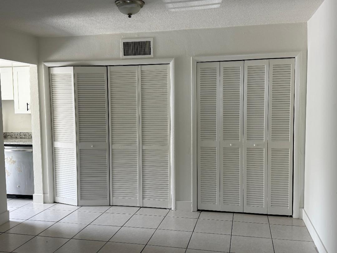 A room with white louvered closet doors, white tile flooring, and a view of a kitchen — 1913 NE 2nd Street # 1, Pompano Beach FL 33060, POMPANO BEACH, FL