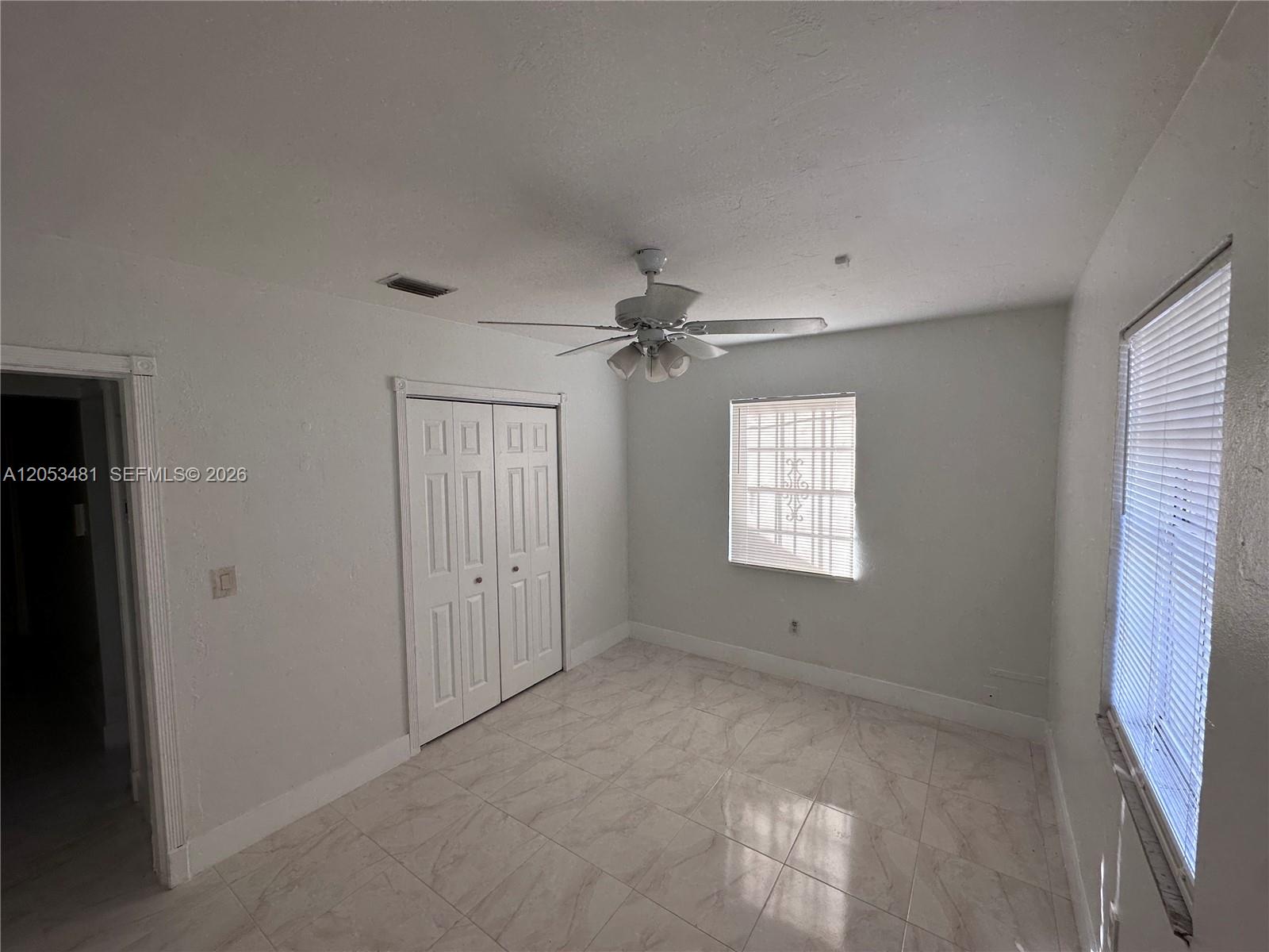 A bedroom with white walls, tiled flooring, a ceiling fan, and two windows with blinds — 1220 NW 53rd St # 1222, Miami FL 33142, MIAMI, FL
