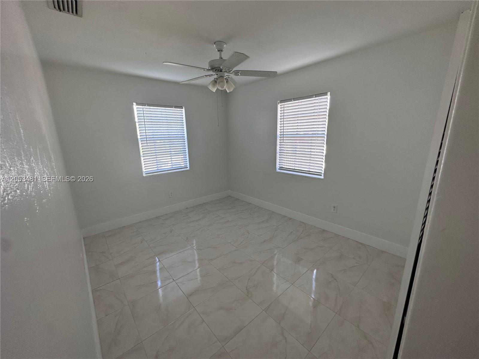 An empty bedroom features white walls, light-colored tile flooring, two windows, and a ceiling fan — 1220 NW 53rd St # 1222, Miami FL 33142, MIAMI, FL