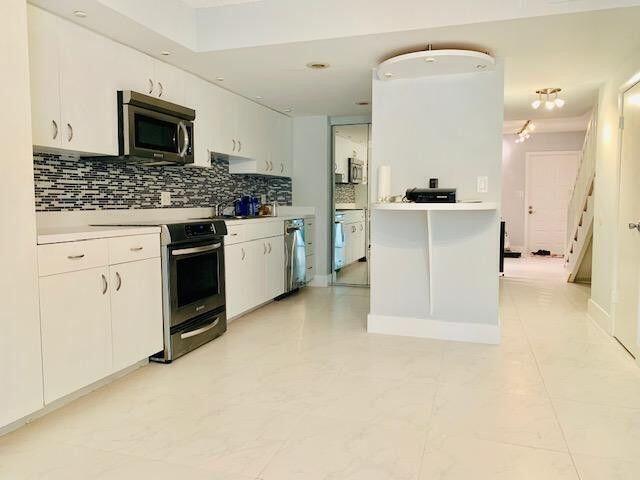 A modern kitchen features white cabinets, stainless steel appliances, and a tiled backsplash — 793 SE 1st Way # 73, Deerfield Beach FL 33441, DEERFIELD BEACH, FL