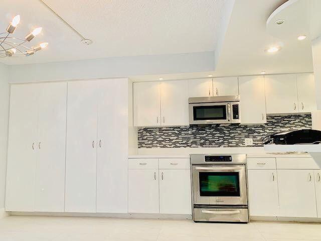 A kitchen features white cabinets, stainless steel appliances, and a dark mosaic tile backsplash — 793 SE 1st Way # 73, Deerfield Beach FL 33441, DEERFIELD BEACH, FL