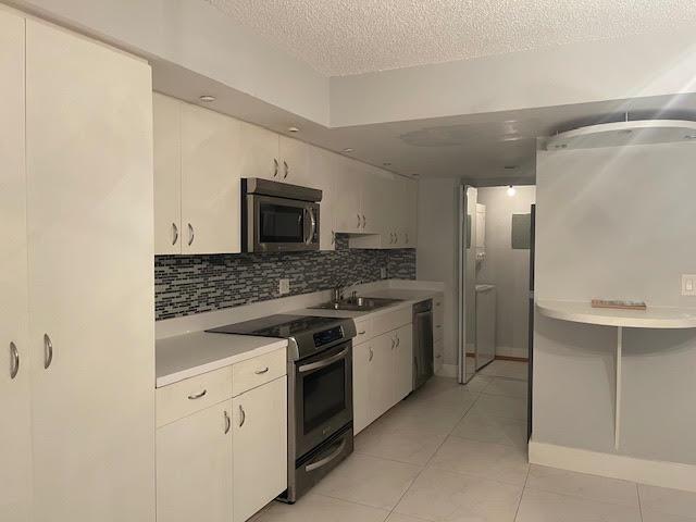A galley kitchen features white cabinets, stainless steel appliances, and a small built-in breakfast bar — 793 SE 1st Way # 73, Deerfield Beach FL 33441, DEERFIELD BEACH, FL