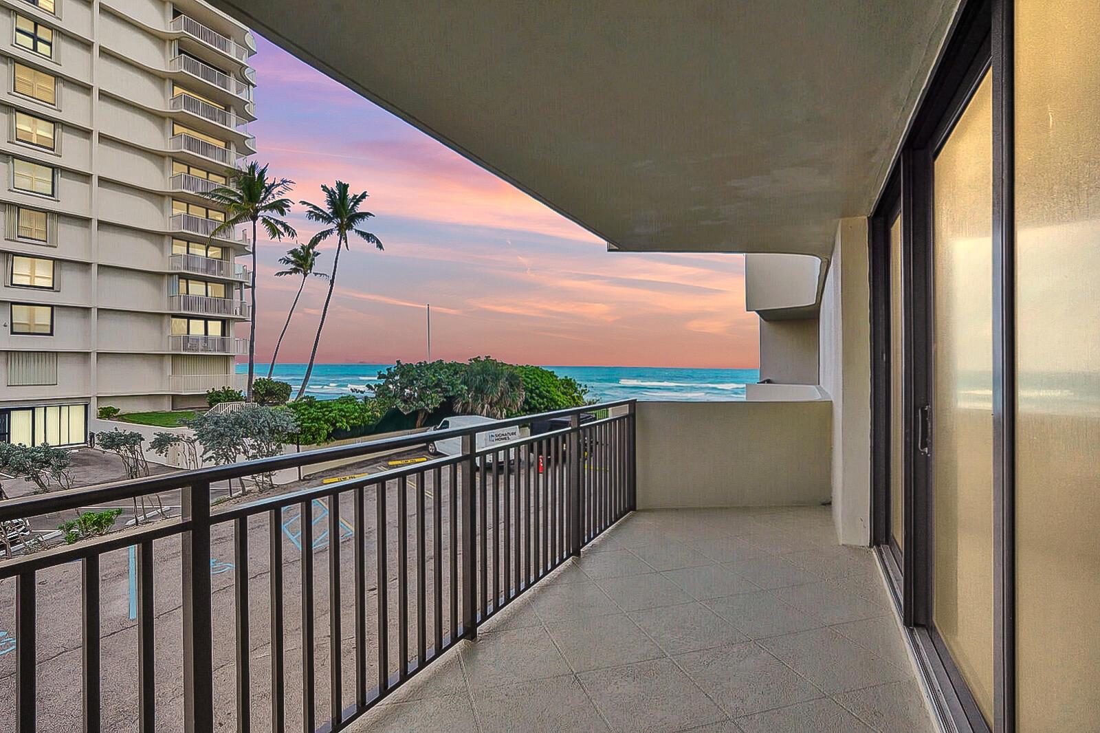 A balcony with a metal railing overlooks a parking lot, palm trees, and the ocean — 5460 N Ocean Drive # 1d, Singer Island FL 33404, SINGER ISLAND, FL