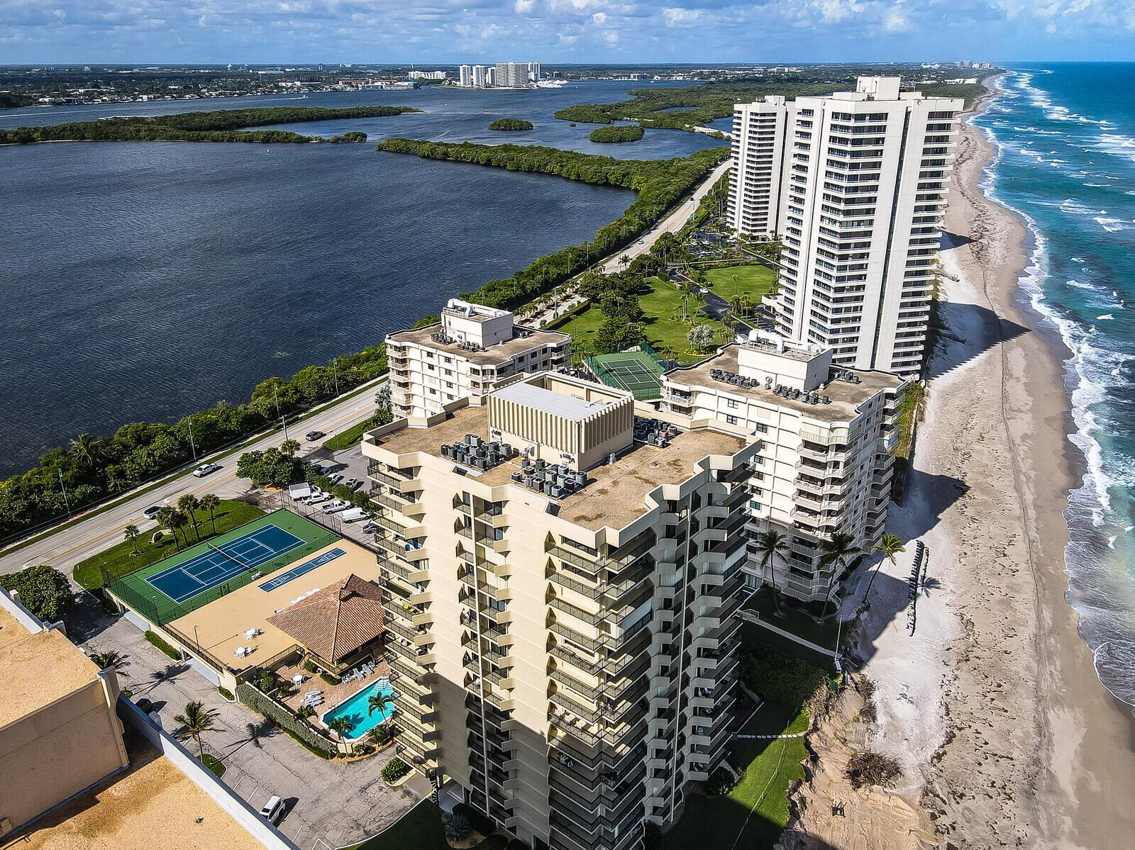 An aerial view shows high-rise residential buildings situated between a coastal beach and a bay — 5460 N Ocean Drive # 1d, Singer Island FL 33404, SINGER ISLAND, FL