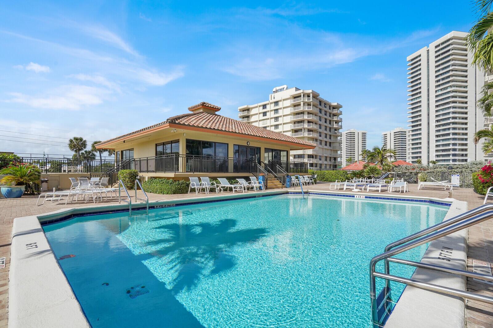 A swimming pool sits in front of a clubhouse building with tall apartment towers nearby — 5460 N Ocean Drive # 1d, Singer Island FL 33404, SINGER ISLAND, FL