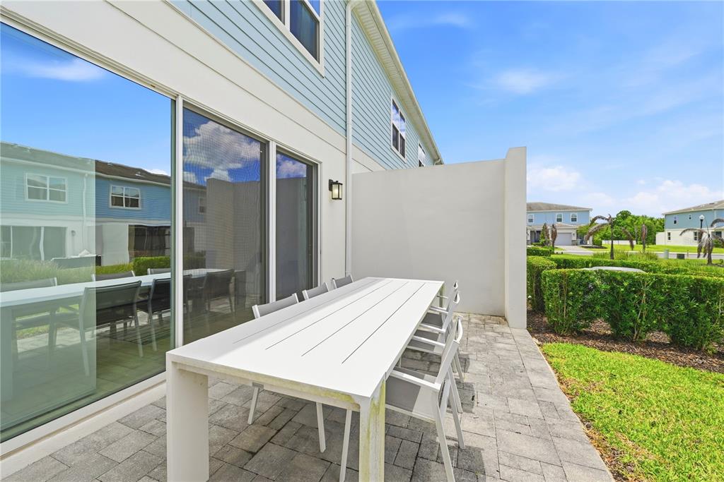 A white outdoor dining table sits on a paved patio beside a light blue house — 7909 DRAW STREET, REUNION, FL