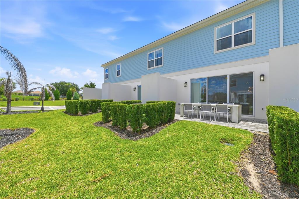 A blue-sided townhouse exterior features a paved patio, outdoor dining set, and manicured hedges — 7909 DRAW STREET, REUNION, FL
