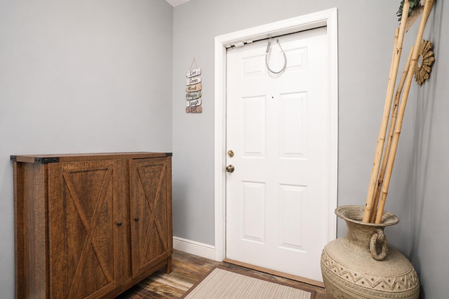 An entryway features a wooden cabinet, a white door with a spring closer, and bamboo stalks — 3314 Concert Lane # 128, Margate FL 33063, MARGATE, FL