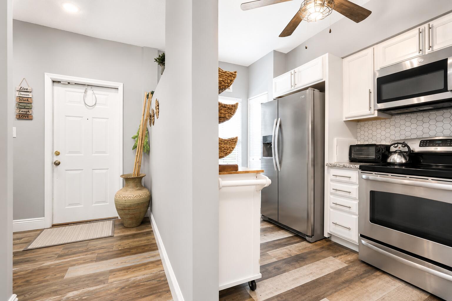 A kitchen with stainless steel appliances and white cabinets opens to an entryway with wood flooring — 3314 Concert Lane # 128, Margate FL 33063, MARGATE, FL