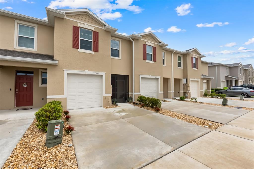 A row of tan townhouses with attached garages and concrete driveways under a blue sky — 1041 LIDO DRIVE, HOWEY IN THE HILLS, FL