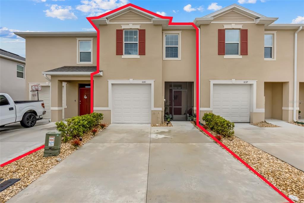 A two-story townhouse exterior features a beige stucco facade, a single-car garage, and red shutters — 1041 LIDO DRIVE, HOWEY IN THE HILLS, FL