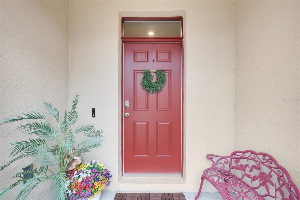 A red front door with a wreath, a potted plant, and a pink metal bench — 1041 LIDO DRIVE, HOWEY IN THE HILLS, FL