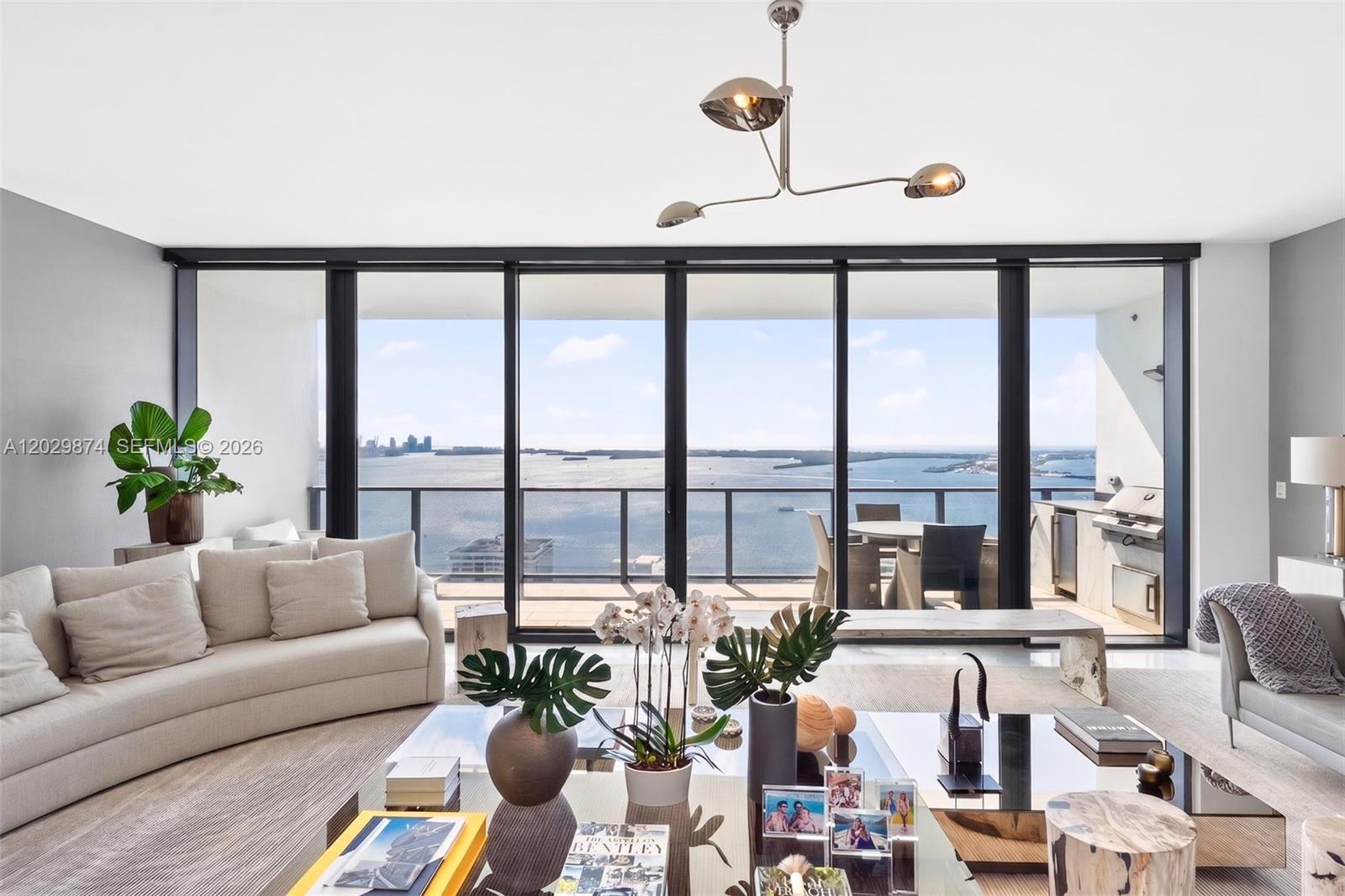A modern living room features a large glass wall overlooking the ocean and a balcony — 1451 Brickell Ave # 2901, Miami FL 33131, MIAMI, FL