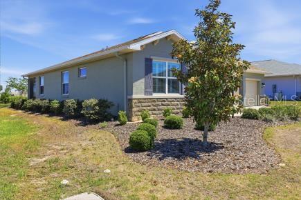 A side view of a single-story house with stone accents, dark shutters, and landscaping — 8907 SW 104TH CIRCLE, OCALA, FL