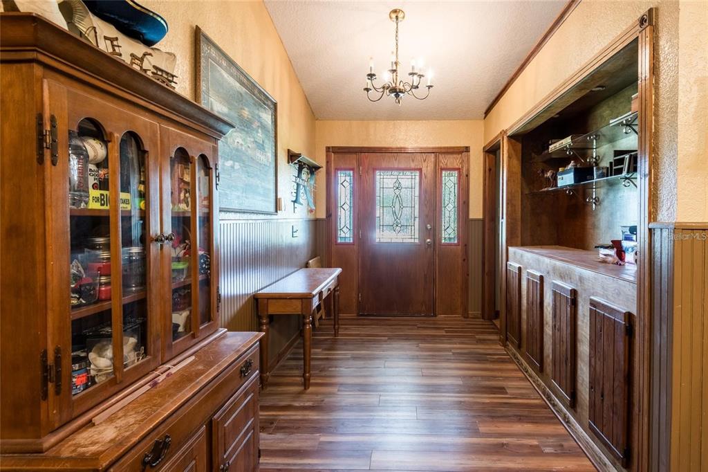 A wood-paneled entryway features a hutch, a built-in bar, a chandelier, and a front door — 11817 MURCOTT WAY, LAND O LAKES, FL