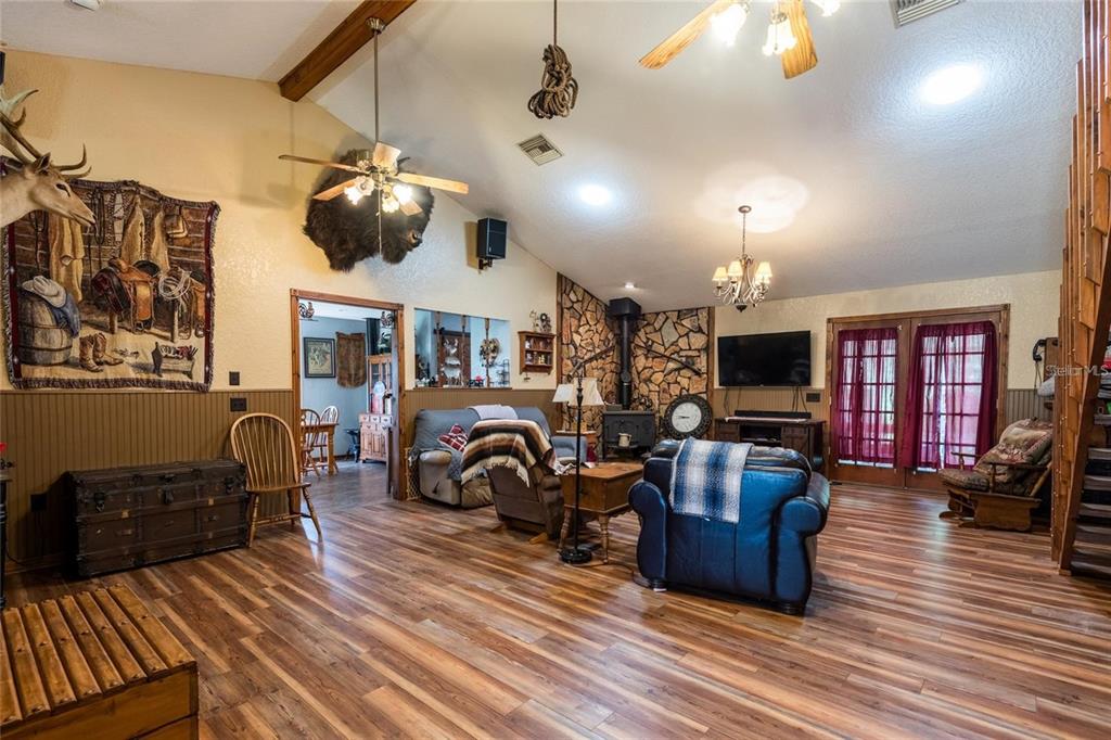 A rustic living room features wood-look flooring, a stone fireplace, and a vaulted ceiling — 11817 MURCOTT WAY, LAND O LAKES, FL