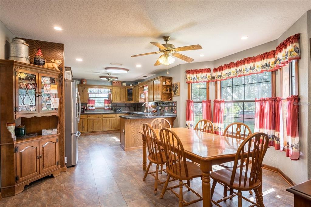 A kitchen and dining area with wooden cabinetry, a wooden table, and rooster-patterned window valances — 11817 MURCOTT WAY, LAND O LAKES, FL