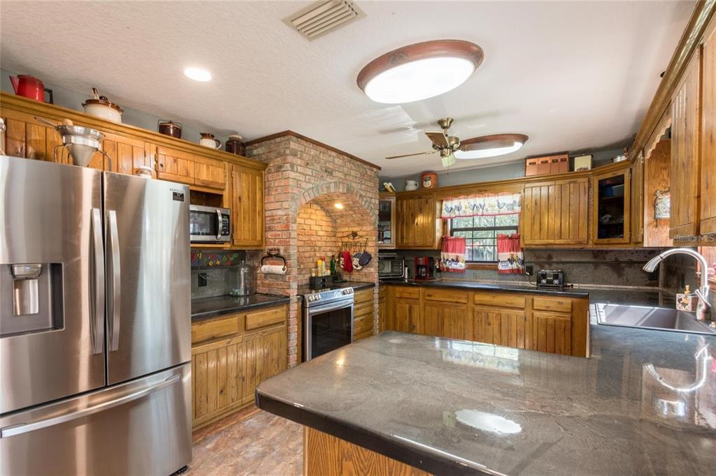 A kitchen features wood cabinets, a brick-enclosed stove area, and dark countertops — 11817 MURCOTT WAY, LAND O LAKES, FL