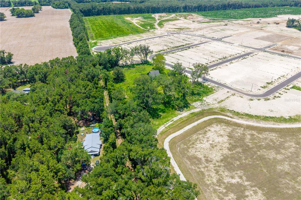 An aerial view shows a house nestled in trees next to a large cleared development site — 23479 W NEWBERRY ROAD, NEWBERRY, FL