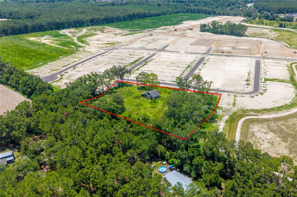 An aerial view shows a house on a wooded lot surrounded by a new development — 23479 W NEWBERRY ROAD, NEWBERRY, FL