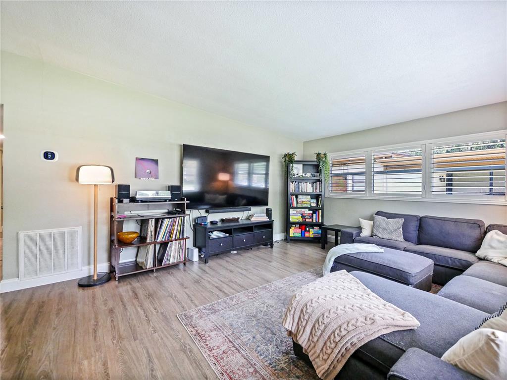 A living room features a large television, a sectional sofa, a bookshelf, and wood-look flooring — 3112 ILLINGWORTH AVENUE, ORLANDO, FL