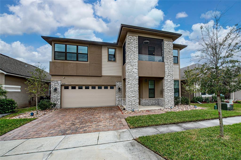 A two-story house features a stone-accented facade, a screened balcony, and a paved driveway — 3018 JARDIN STREET, KISSIMMEE, FL