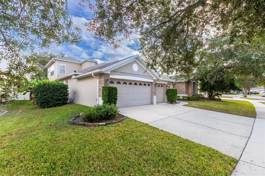 A beige house with a three-car garage and a concrete driveway under large oak trees — 13157 PALOMA DRIVE, ORLANDO, FL