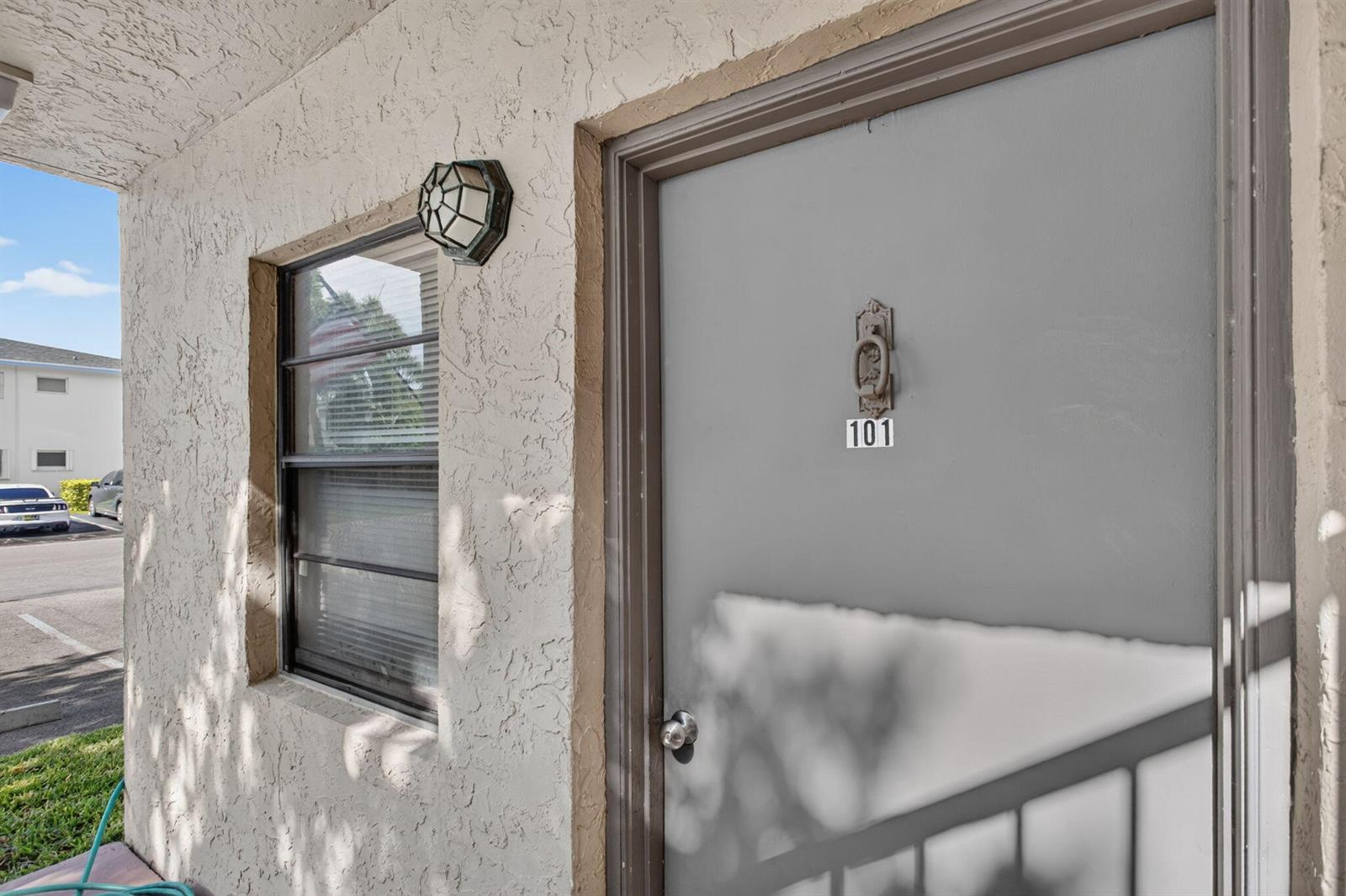 A view of an apartment entrance with a gray door numbered 101 and a window — 2141 NE 42nd Street # 101, Lighthouse Point FL 33064, LIGHTHOUSE POINT, FL