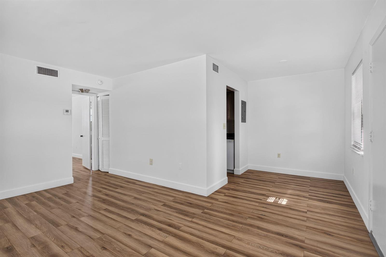 An empty room with white walls, wood-look flooring, and a doorway leading to a kitchen — 2141 NE 42nd Street # 101, Lighthouse Point FL 33064, LIGHTHOUSE POINT, FL