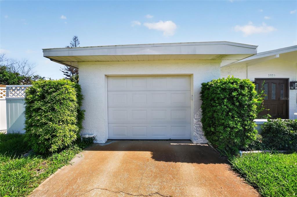 A white garage with a single door is flanked by large green bushes — 2525 CORAL WAY W, DAYTONA BEACH, FL