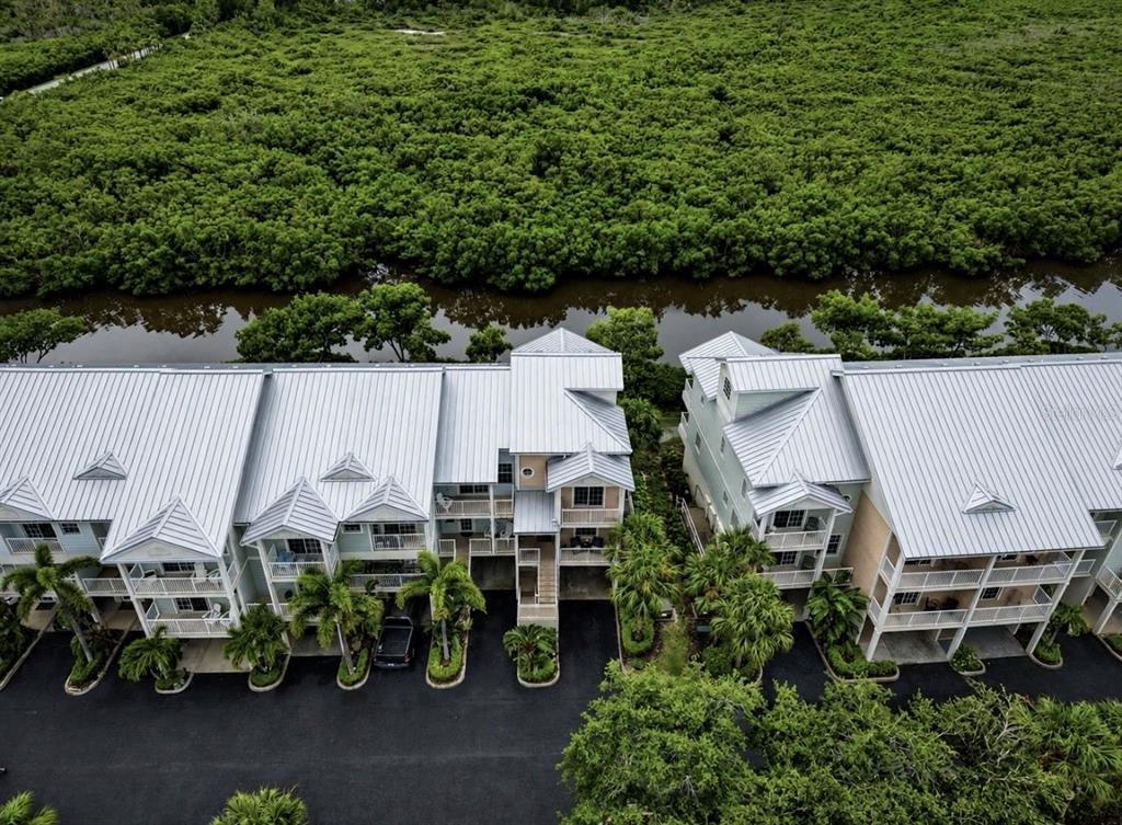 An aerial view shows two multi-story residential buildings with metal roofs next to a waterway — 3228 MANGROVE POINT DRIVE, RUSKIN, FL