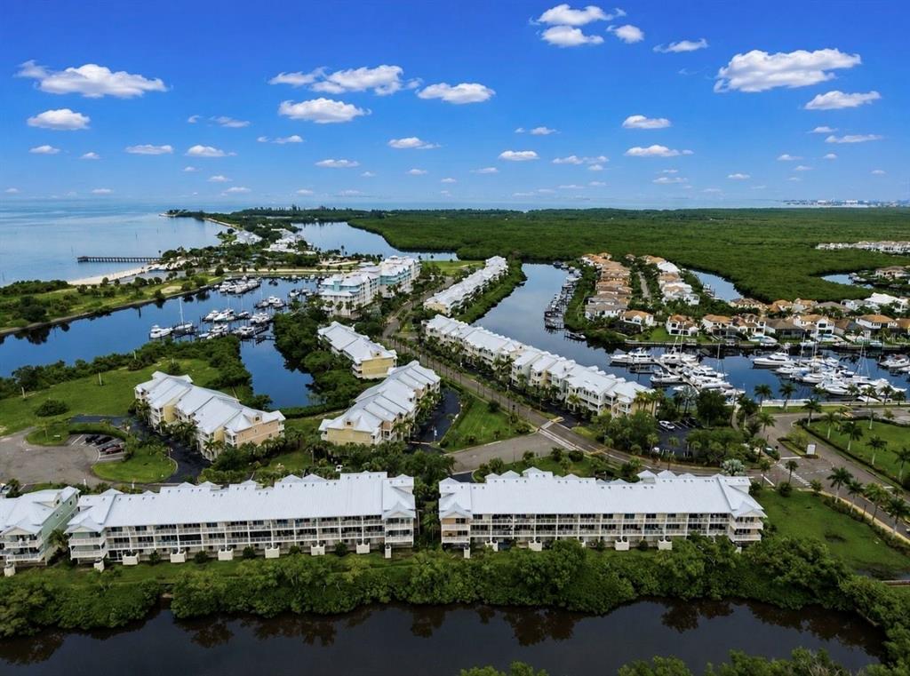 An aerial view shows waterfront residential buildings, boat slips, and lush vegetation along the coast — 3228 MANGROVE POINT DRIVE, RUSKIN, FL