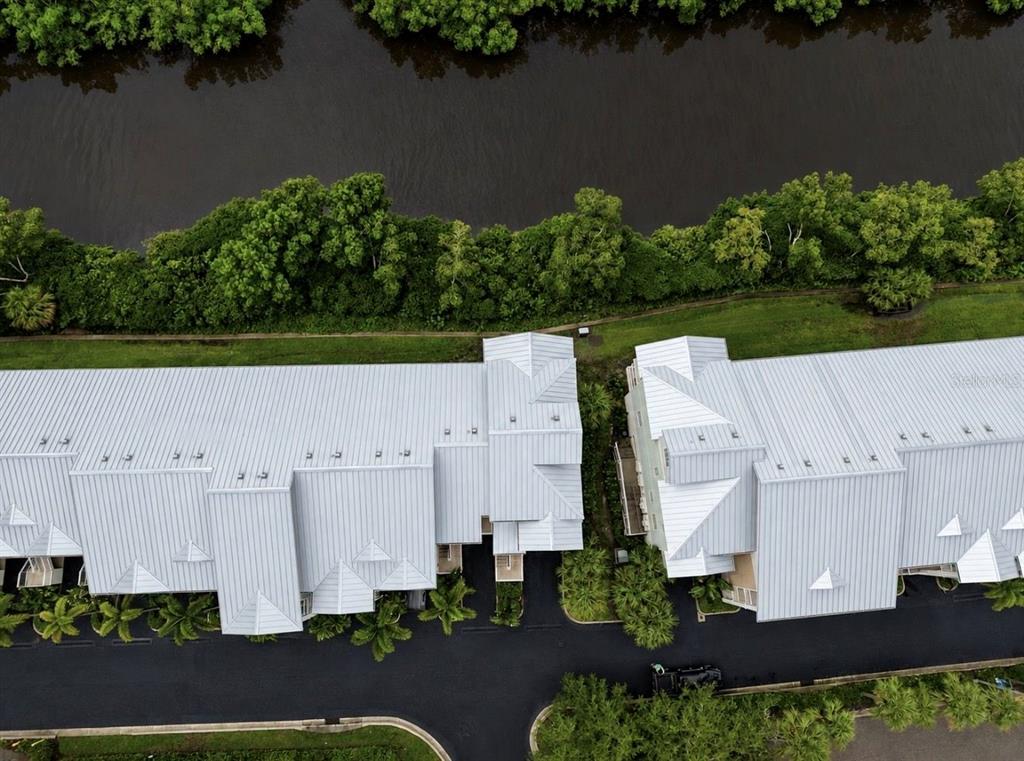 An aerial view shows two multi-story townhomes with metal roofs situated beside a narrow waterway — 3228 MANGROVE POINT DRIVE, RUSKIN, FL